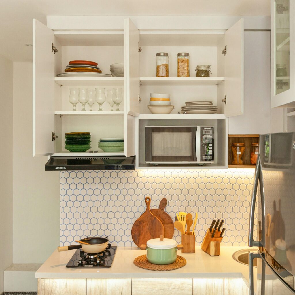pexels-photo-5556176-5556176 A stylish kitchen showcasing open cabinets with dishes, cookware, and modern appliances.